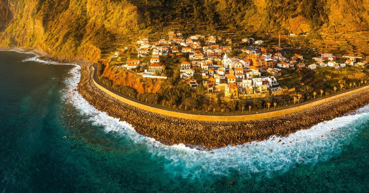 Vista aérea do casario do Jardim do Mar ao pôr do sol, junto ao paredão e ao mar.